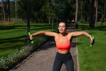 Young sporty woman exercising with dumbbell standing on a running way in the urban park