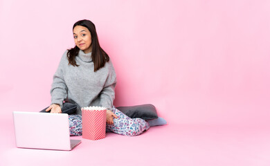 Young mixed race woman eating popcorn while watching a movie on the laptop happy and smiling