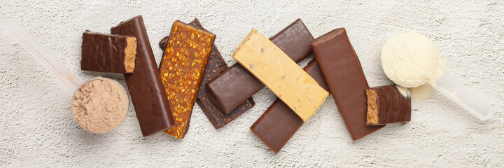 Whey protein powder in measuring scoop and different energy protein bar on grey background.