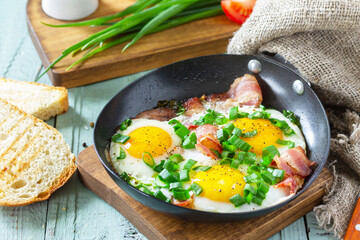 Spring scrambled eggs with green onions and bacon in a cast iron skillet on a rustic wooden background.