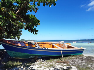 Small fishing boat beached on shore with turquoise waters of the Caribbean Sea and tropical blue sky. Close up of traditional fishing boat. French Antilles background.