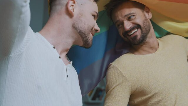 Close up, homosexual male couple having fun and flirting covered with rainbow flag. High quality 4k footage