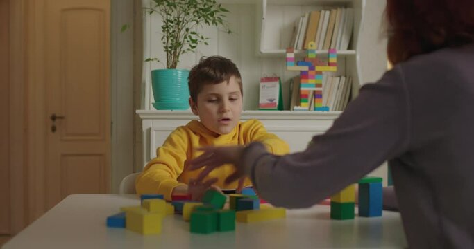 Autistic boy building with color wooden blocks. Teacher gives assignment to pupil with autism. Applied behavior analysis therapist working with kid.