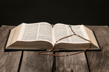 Holy bible open on rustic wooden table in dark night.