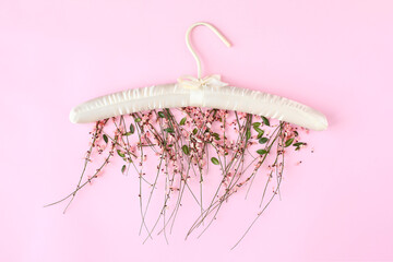 Clothes hanger with flowers on pink background.