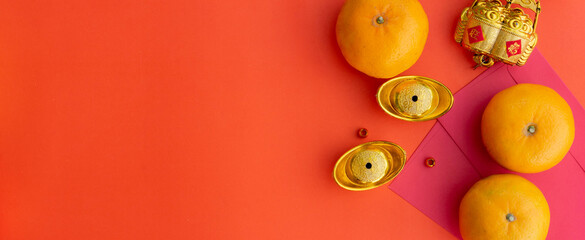 close up gold ingots , oranges fruit and red envelope pocket (ang pao) over orange  color background table for special chinese new year traditional and culture concept