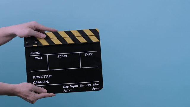 Movie Clapperboard. Film crew man hold and move up film slate in to the frame and clap it and move down out of the frame. yellow and black stripe clapperboard isolated blue background Video production