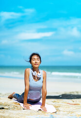 Fototapeta na wymiar A beautiful woman doing yoga on the rocks at the beachside.