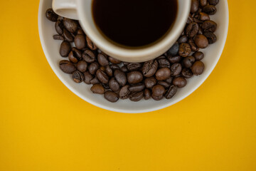 A photo of a half coffee cup surrounded by coffee beans on a plate on a yellow background