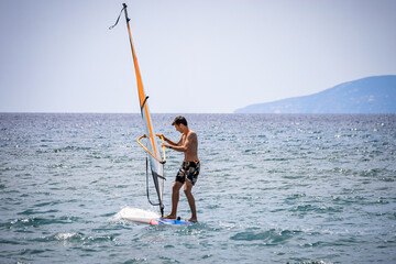Young man trying to steer his windsurf on an open sea