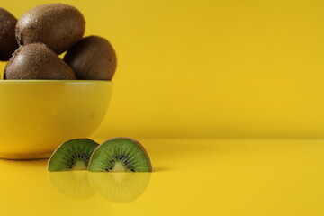 Still life fruit in a yellow bowl plate on a yellow background next to lies a piece of kiwi illuminatiited yellow trend color copyspace