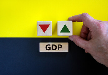 GDP, gross domestic product symbol. Businessman holds a cube with up icon. Wooden block with word 'GDP'. Beautiful yellow and black background. Copy space. Business and growth of GDP concept.