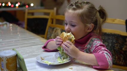 Little girl eating hamburger. Child with hamburger watching cartoons on smartphone