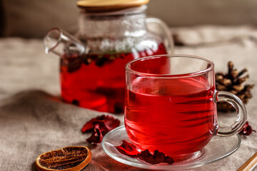 Red tea brewed in glass tea pot and a cup of red tea on beige background. Closeup. Healthy nutrition concept