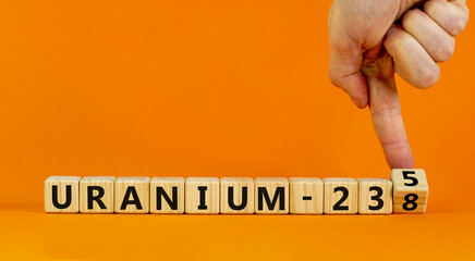Uranium enrichment symbol. Hand turns cube and changes words 'uranium-238' to 'uranium-235'. Beautiful orange background, copy space. Business, nuclear technology and uranium enrichment concept. - obrazy, fototapety, plakaty