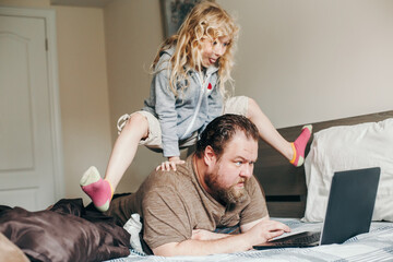 Work from home with kids children. Father working on laptop in bedroom with child daughter on his back. Funny candid family moments. New normal during coronavirus quarantine lockdown. - 403865645