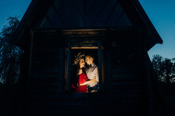 Loving couple at the window of a whimsical house at night, lake countryside