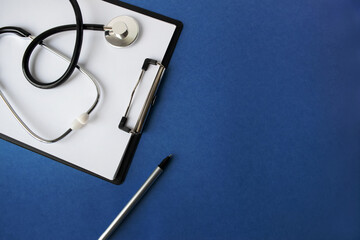 Doctor's workplace. Top view on a blue background with medical equipment - stethoscope, tablet with a blank sheet of paper, glasses. Medical concept.