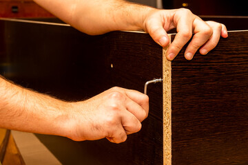 men's hands assemble furniture with a hex key made of dark brown laminated chipboard