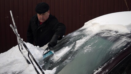 Fototapeta na wymiar A man cleans a car windshield from snow with a brush. Winter in Russia, the car was covered with snow