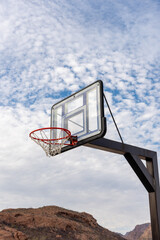 Naklejka premium Basketball hoop and clear see-through backboard in the desert against a cloudy sky with patches of blue.