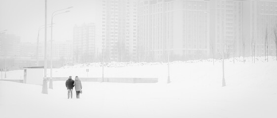 An adult couple walks through a snowy city. horizontal, monochrome Loneliness in a big city.