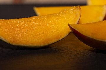 Sliced mango slices close up on a black background. The concept of healthy vitamin fruit