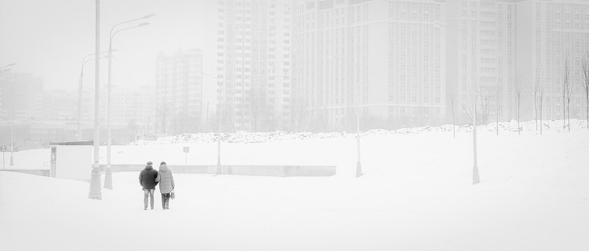 An adult couple walks through a snowy city. horizontal, monochrome Loneliness in a big city.