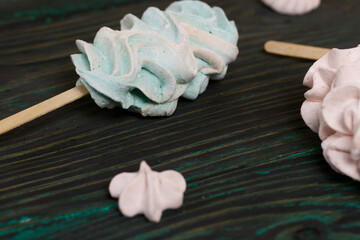 Zephyr on a stick. Nearby are marshmallow stars of different shades. Close-up shot. Against a background of black-green pine boards.