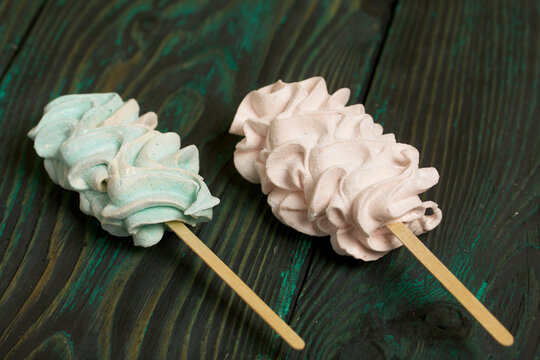 Zephyr on a stick. Marshmallows of different shapes and shades. Close-up shot. Against a background of black-green pine boards.