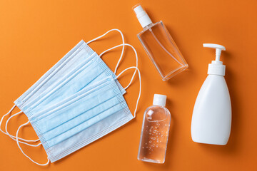 Medical protective, face masks, sanitizer gel, spray, liquid hand soap on orange background, close-up, flatly, minimal. Hygiene concept, protective equipment, prevention of spread of viral infections