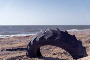Fototapeta premium An image of an old car tire ingrown into the sand. Old car tire lying on the beach.