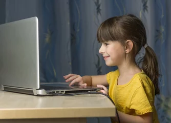 Fotobehang .Online onderwijs op afstand. Een gelukkig meisje kijkt naar laptop en glimlacht © Albert Ziganshin