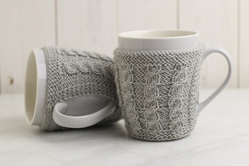 Teacups in decorative sweaters on light background