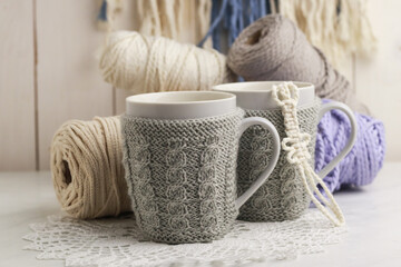 Teacups in decorative sweaters on light background