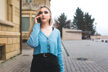 Fototapeta premium Young blonde woman taking by mobile phone on the street