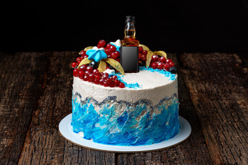 Festive fruit cream cake with a bottle of cognac, on a wooden textured background.