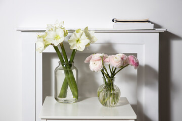 A bouquet of pink Persian buttercups in a glass vase and two wrapped gifts on a white table in front of a fake white fireplace.
