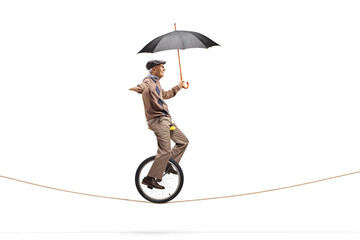 Full length profile shot of an elderly man riding a unicycle on a rope and holding an umbrella © Ljupco Smokovski