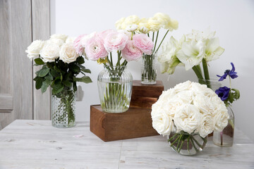 White roses, ranunculus, blue anemones, yellowish buttercups, lilies in round vases on the wooden boxes on the table for a special occasion