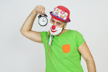 The clown holds an alarm clock in his hands. Isolated on white
