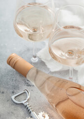 Glasses and bottle of rose pink wine with steel corkscrew on light background.