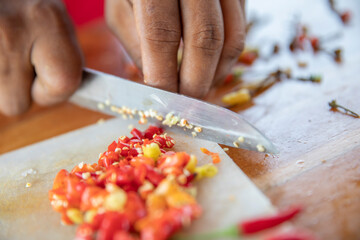 close up of a hand cutting white onions and chilli pepper on a kitchen board with a knife