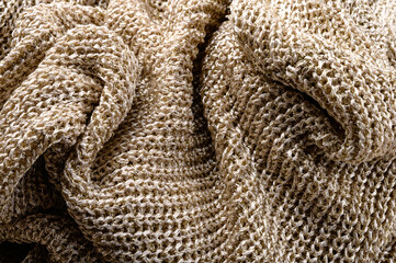 Background of knitted crumpled fabric in gold color close-up.