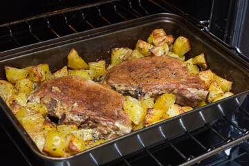 Two pork entrecotes with potatoes baked in the oven. Homemade food in the oven. Baked meat with...