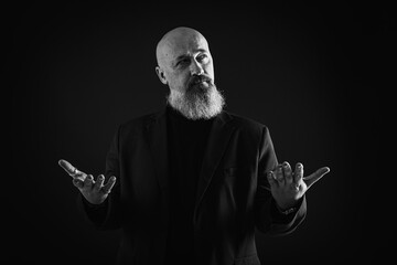 Smiling business man with beard showing man, gesturing with hands, showing something, isolated on dark background. Low key. The portrait is emotional