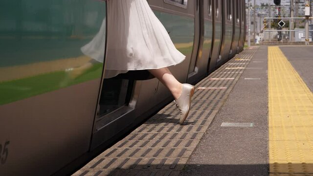 Tourist woman get on Japanese rapid transit train, low half shot of female legs walking to vehicle door. Empty platform at terminal station, train wait for first passengers
