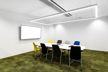 Mała sala konferencyjna w korporacji z monitorem na ścianie, krzesłami, stołem oraz zieloną podłogą - obrazy, fototapety, plakaty