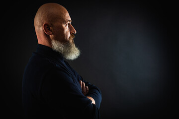 close up photo, portrait of a serious, thoughtful, bearded man on a dark background looking...