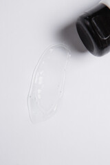 drop of transparent gel is smeared on a white background next to a closed tube of gel